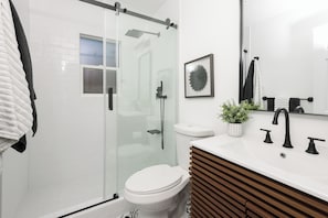 Une salle de bain moderne avec une douche à parois de verre, des toilettes blanches et un meuble-lavabo en bois avec un évier.