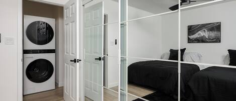 Un dormitorio moderno con separador de vidrio, lavadora y cama con ropa de cama negra.