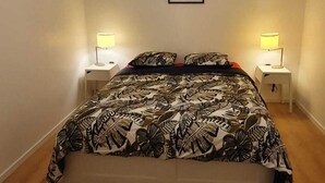 A bedroom with a bed, two bedside tables, a nightstand, a framed picture on the wall, and a brown rug.