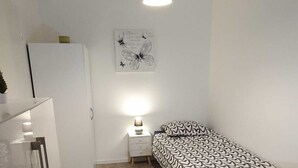 A small, well-lit bedroom with a bed, bedside table, and a hanging light fixture.