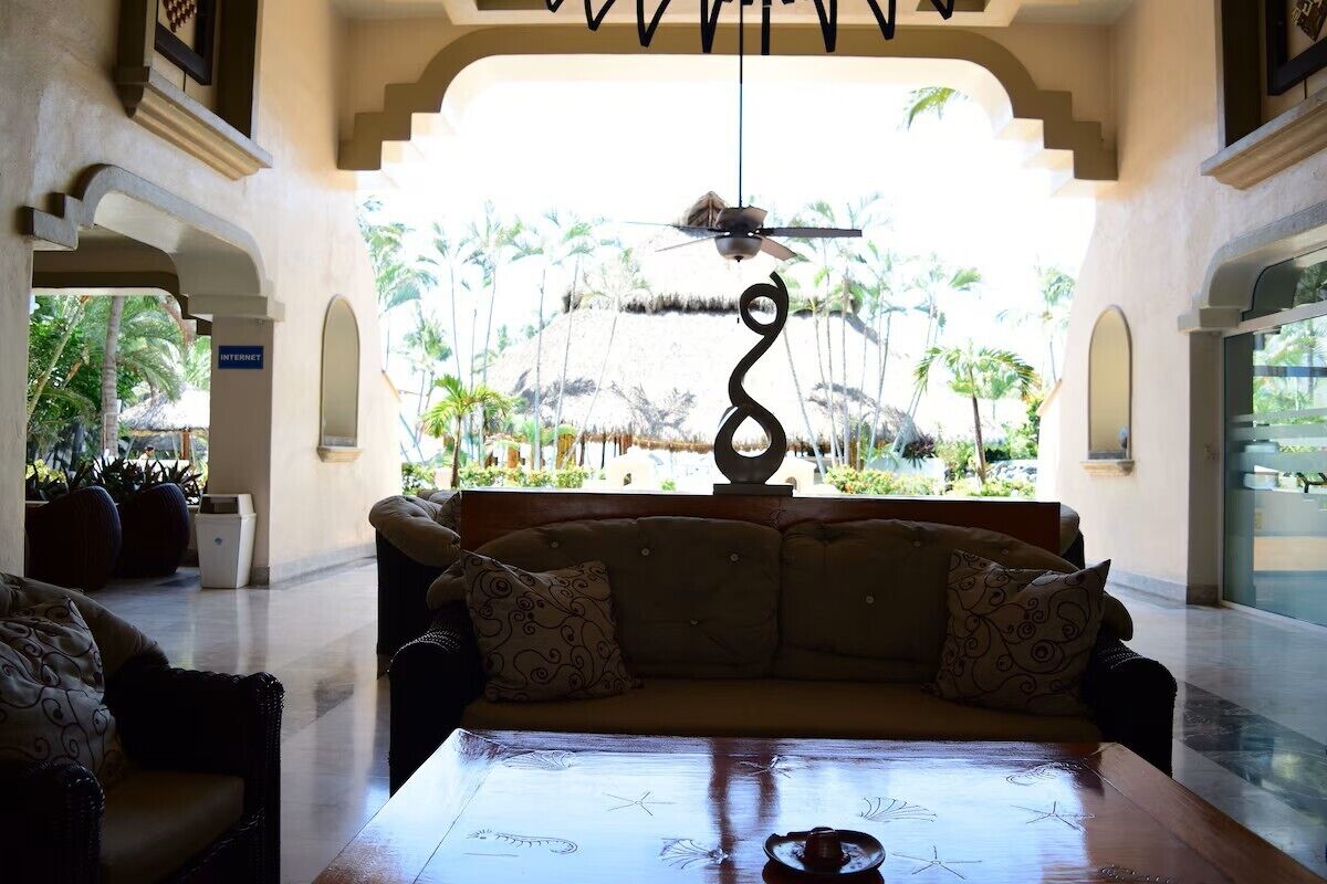 A lobby with a sofa, a table with a teapot, and a ceiling fan.