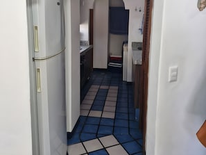A narrow hallway with a tiled floor, leading to a kitchen area with cabinets and a countertop.
