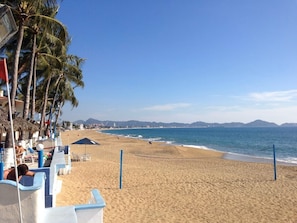 A beach with a netted volleyball court, palm trees, and beach chairs.