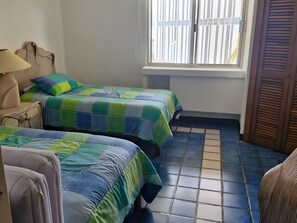 A room with two beds, a chair, a lamp, and a window with blinds. - GRAN PACIFICO, OCEANFRONT CONDOMINIUM, MANZANILLO (Manzanillo)