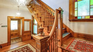 A grand wooden staircase with a chandelier, a fire exit sign, and a patterned rug. - 2-Acre Property: Victorian Home in Brownville! (Brownville)