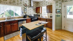 A kitchen with wooden cabinets, a central island, and a window overlooking greenery. - 2-Acre Property: Victorian Home in Brownville! (Brownville)