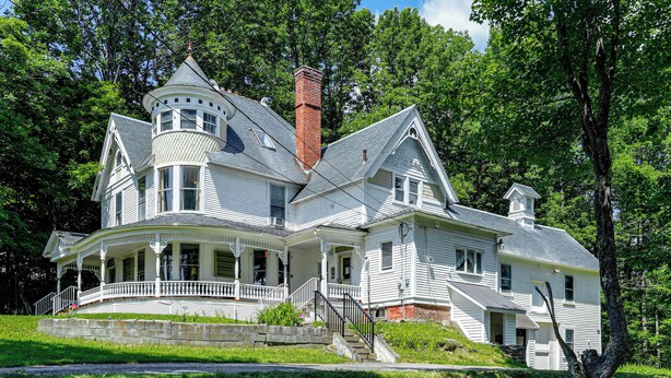 A large, white, two-story house with a wrap-around porch, a turret, and a chimney. - 2-Acre Property: Victorian Home in Brownville! (Brownville)