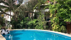 A swimming pool surrounded by lush greenery and residential buildings. - Cozy apartment in tropical villa surrounded by trees. Oasis in the city! (Cancún)