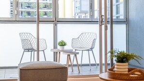 A modern balcony with two wireframe chairs, a small round table, and a potted plant.