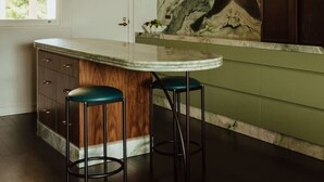 Une cuisine moderne avec un îlot en marbre, des meubles de couleur verte et deux tabourets.