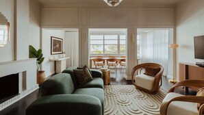 Un salon spacieux avec un canapé vert, des fauteuils en osier, une cheminée et une grande fenêtre.