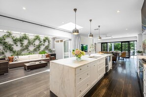 A modern kitchen with a central island, a dining area with a table and chairs, and a living area with a sofa and coffee table. - Iris @ Norwood—Luxe Indoor-Outdoor Living near CBD (Norwood)