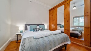 Et soveværelse med et stort spejl, en seng med et stribet tæppe og et natbord med en lampe.