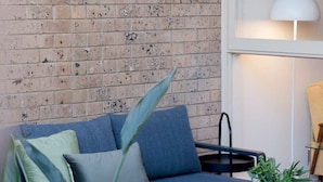 A modern living room with a blue sofa, a coffee table, and a potted plant. - Honeyeater Hidden Gem—Stylish Courtyard in the CBD (North Adelaide)