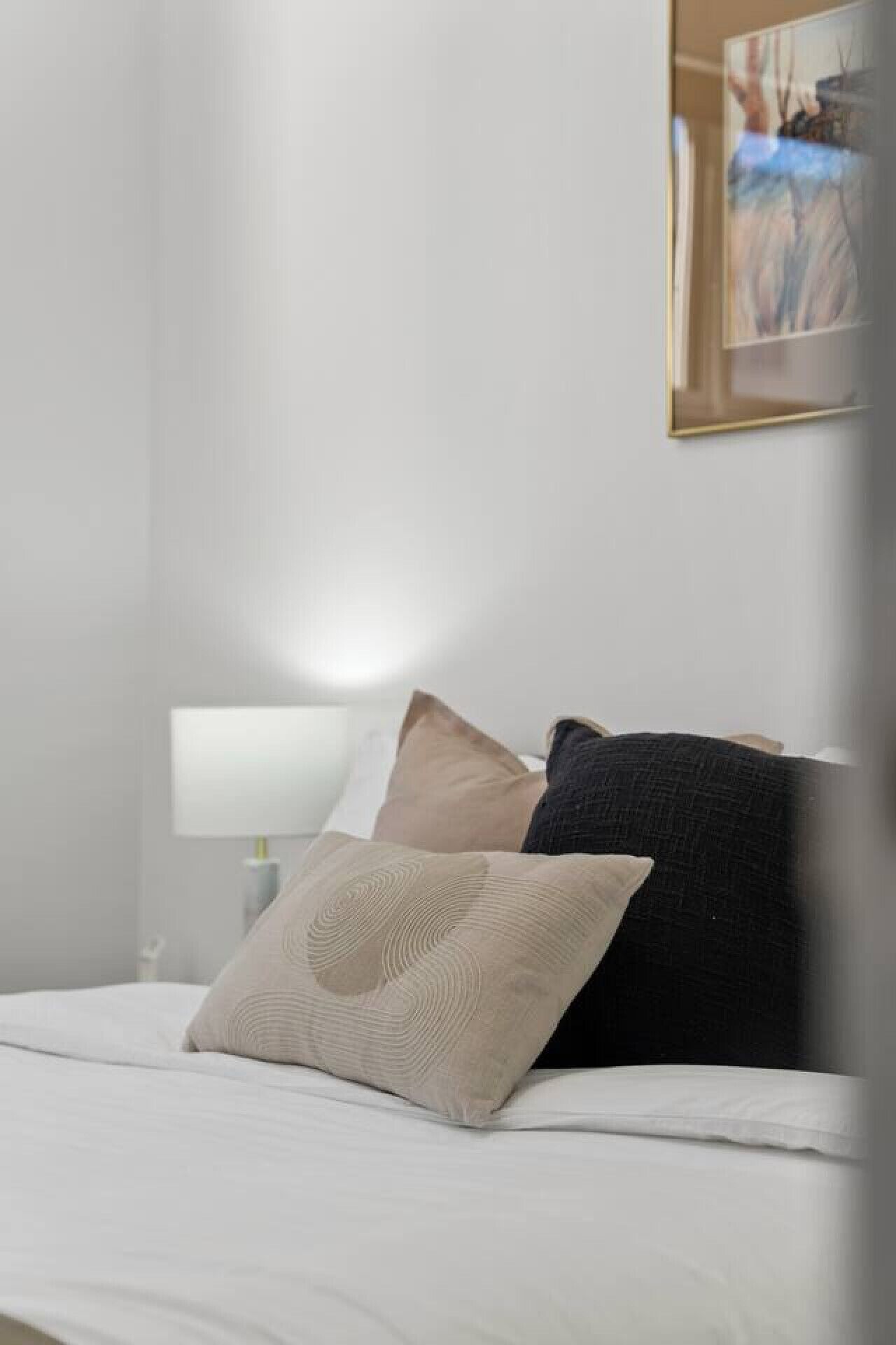 A neatly made bed with two pillows, a bedside lamp, and a framed picture on the wall.