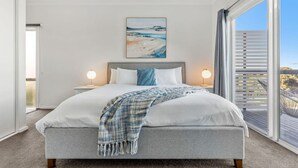 Ein Schlafzimmer mit einem großen Bett, zwei Nachttischlampen, einem Bild über dem Bett und einem Balkon mit Blick.