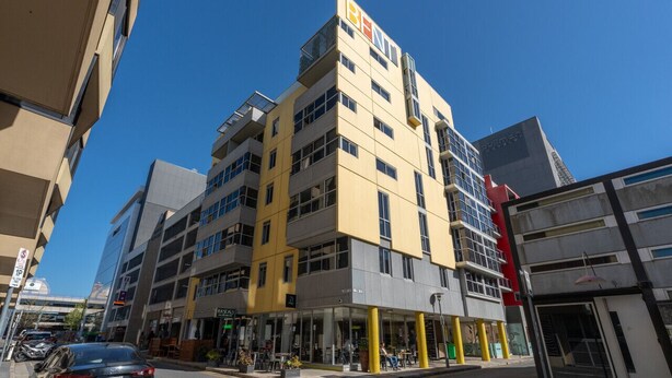 A multi-story building with a yellow and grey facade, multiple balconies, and a ground-level entrance with a covered area. - Artful Escape on York - Walkable Location in the CBD (Adelaide)