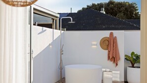 Un baño al aire libre moderno con ducha independiente, bañera redonda y una planta en maceta.
