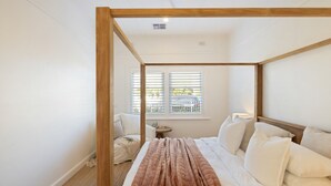 Una cama con dosel de madera, ropa de cama blanca y vistas a un balcón por la ventana.