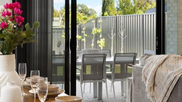 A dining area with a table set for four, a sofa, and a view of the backyard through a sliding glass door. - Paradise Palms—Modern Coastal Escape with Backyard (Aldinga Beach)