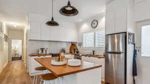 A modern kitchen with white cabinets, a stainless steel refrigerator, wooden bar stools, and pendant lighting.