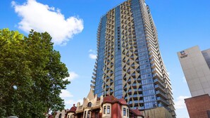 A tall, modern building with a geometric facade and a clear blue sky in the background.