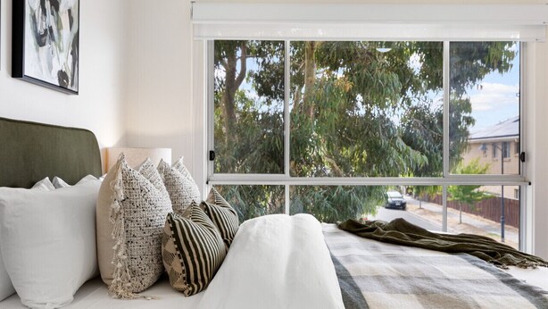 A bedroom with a large window, a bed with white bedding, and several pillows. - Mawson Lakes Retreat—A Peaceful and Prime Location (Mawson Lakes)