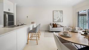 A modern kitchen with white cabinetry, a built-in island, and a dining area with a round table and chairs. - Mawson Lakes Retreat—A Peaceful and Prime Location (Mawson Lakes)