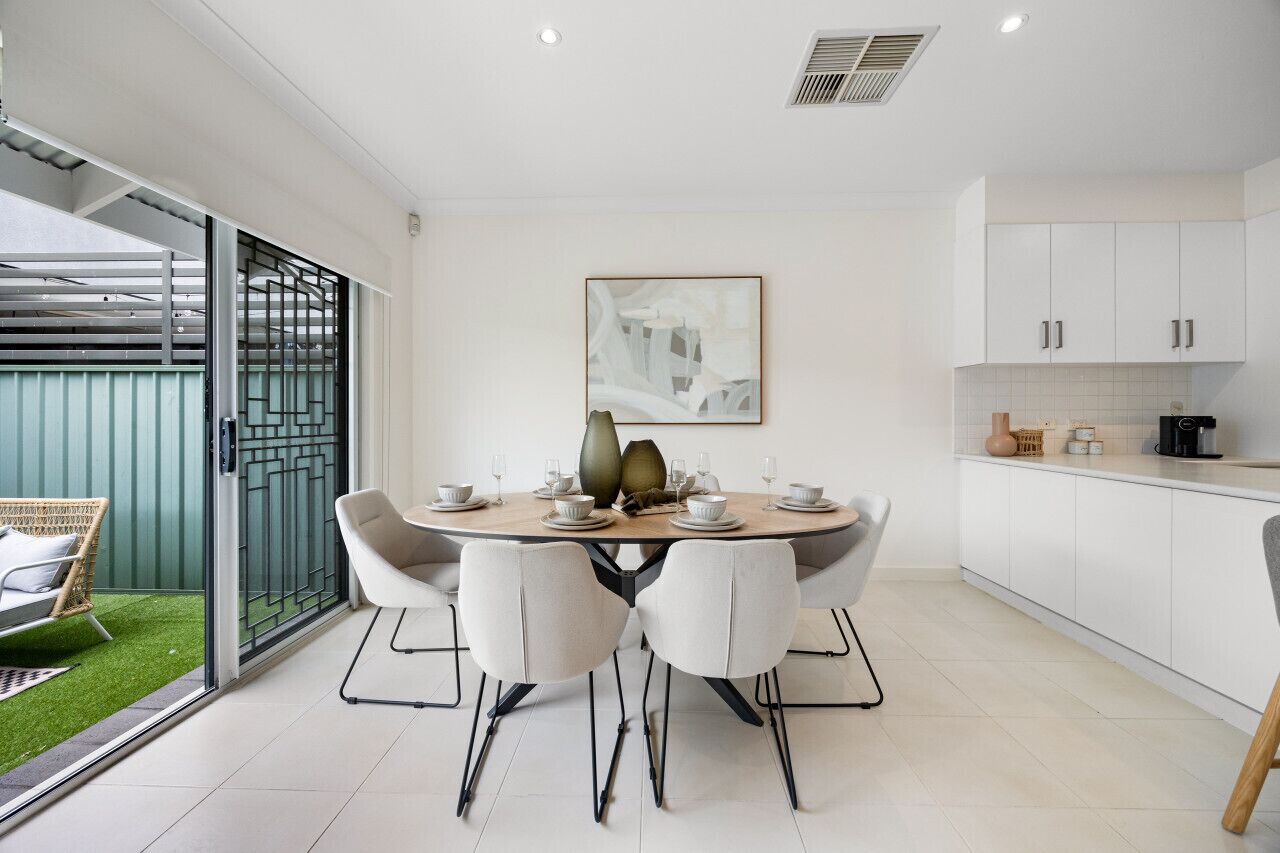 Una cocina moderna con armarios blancos, una mesa de comedor lista para cuatro personas y un puerta corrediza de vidrio que da a un balcón.