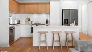 Une cuisine moderne avec des meubles en bois, un îlot central doté de tabourets, un réfrigérateur encastré et un lave-vaisselle.