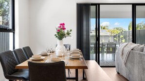 Un coin repas avec une table en bois dressée pour six personnes, des chaises noires à revêtement en tissu et un vase blanc orné de fleurs roses.