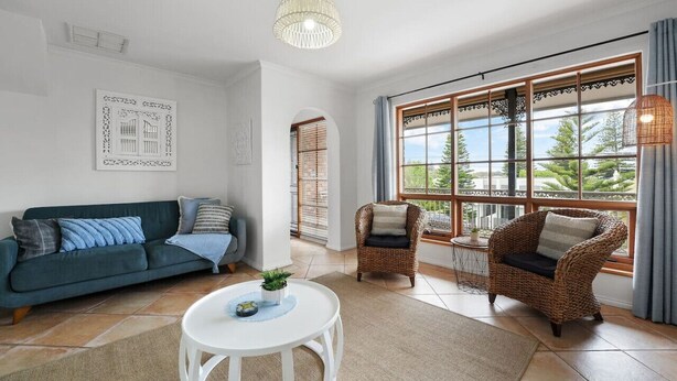 Una sala de estar con un sofá, dos sillones de mimbre, una mesa redonda y un ventanal con vistas a zonas verdes.