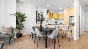 A modern kitchen with wooden cabinets, a dining area with a dark table and grey chairs, and a potted plant.