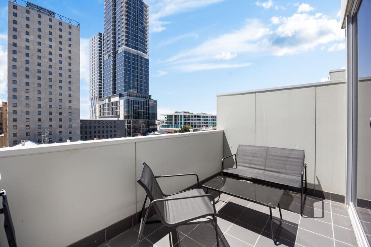 A balcony with two chairs and a table, overlooking a cityscape with modern buildings.