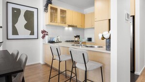 A modern kitchen with wooden cabinets, a central island with bar stools, a framed artwork, and a vase with flowers.