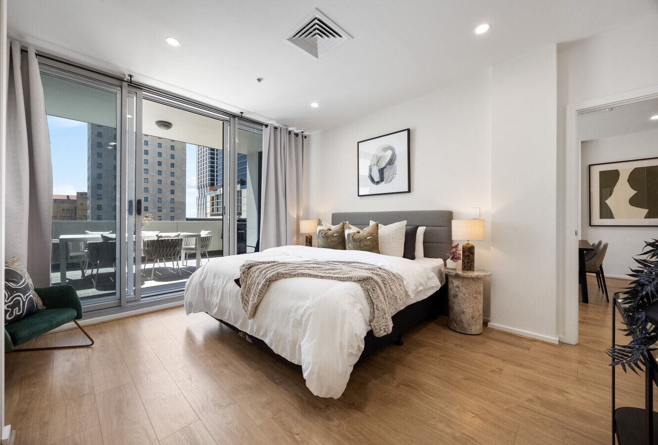 A modern bedroom with a large bed, a glass door leading to a balcony, and a city view.