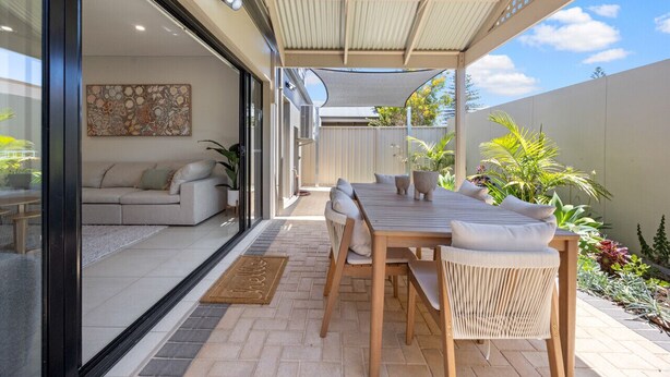 A covered patio with a wooden table and chairs, a sofa, and a potted plant.