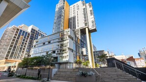 A modern high-rise building with multiple floors, large windows, and a prominent yellow accent. - The Balfours Haven - City Views & Balcony (Adelaide)