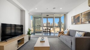 A modern living room with a flat-screen TV, a coffee table, a sofa, and a balcony with a city view. - The Balfours Haven - City Views & Balcony (Adelaide)