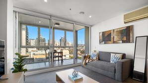 A modern living room with a grey sofa, a wooden coffee table, and a city view through large sliding glass doors. - The Balfours Haven - City Views & Balcony (Adelaide)