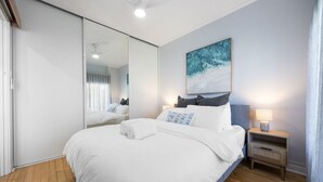 A bedroom with a large bed, a nightstand with a lamp, a wall-mounted painting, and a sliding door. - Brighton Breeze Retreat—Idyllic Beachside Stay (Brighton)