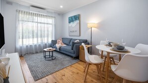 A modern living room with a sofa, a dining table with chairs, a small rug, and a painting on the wall. - Brighton Breeze Retreat—Idyllic Beachside Stay (Brighton)