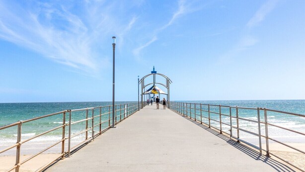 A pier extending into the sea with a metal railing on both sides and a covered area at the end. - Brighton Breeze Retreat—Idyllic Beachside Stay (Brighton)