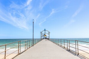 A pier extending into the sea with a metal railing on both sides and a covered area at the end. - Brighton Breeze Retreat—Idyllic Beachside Stay (Brighton)