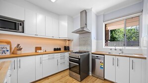 A modern kitchen with white cabinets, a stainless steel stove, and a dishwasher. - Brighton Breeze Retreat—Idyllic Beachside Stay (Brighton)