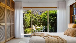 A bedroom with a large bed, a view of a garden through a sliding glass door, and a wooden wardrobe. - Amber Wisper—In the Hills with Pool & Tennis Court (Paechtown)