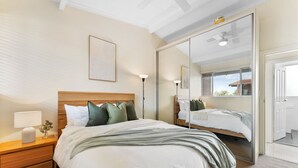 Une chambre moderne avec un grand lit, une table de chevet avec une lampe, une petite table de chevet avec un vase et un grand miroir.