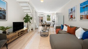 Een moderne woonkamer met een flatscreen televisie, een bank en een eethoek met een tafel en stoelen.