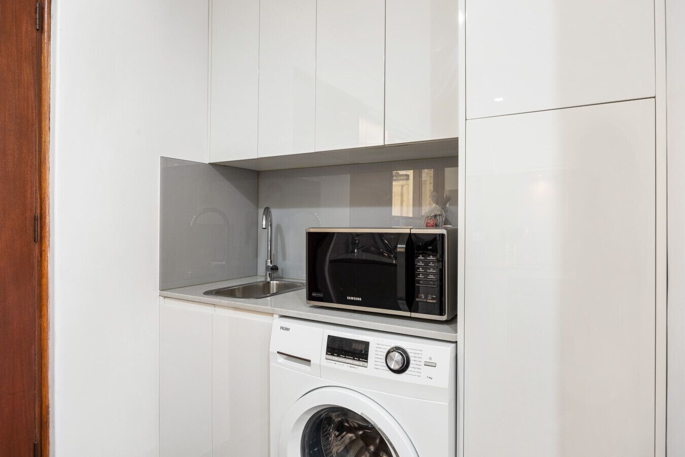 Une cuisine compacte équipée d’un four à micro-ondes encastré, d’un évier et d’un lave-linge à chargement frontal.