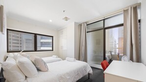 Ett hotellrum med två sängar, ett skrivbord och ett stort fönster med gardiner.